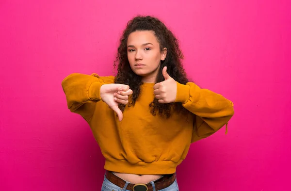 Teenager girl over pink wall making good-bad sign. Undecided between yes or not