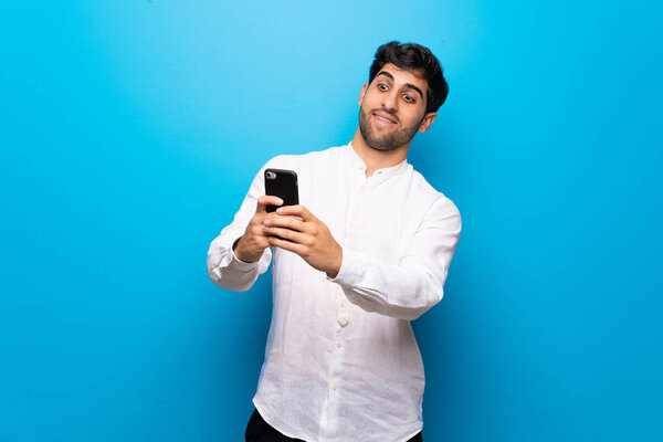 Young man over isolated blue wall making a selfie