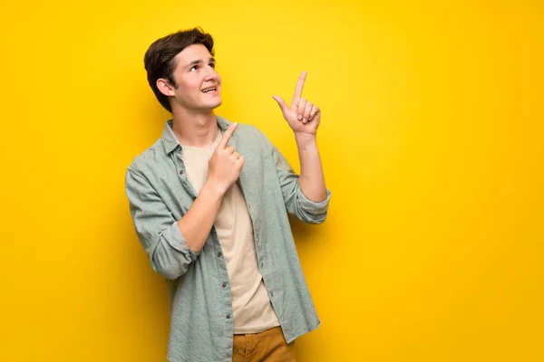 Nastolatek Mężczyzna Nad Żółte Ściany Wskazując Palcem Wskazującym Patrząc Górę — Zdjęcie stockowe