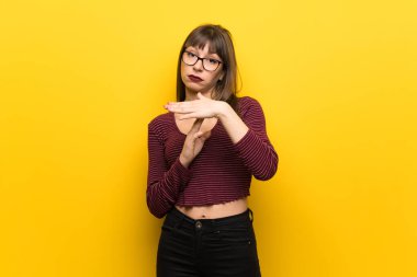 Sarı duvar üzerinde gözlük olan kadın zaman aşımına jest yapma