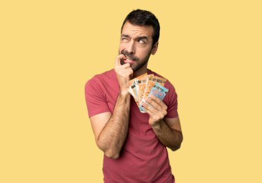 İzole sarı arka plan üzerinde bakarak zaman şüpheli sahip bir sürü para alarak adam