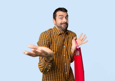 Alışveriş çantaları ile adam mutsuz ve izole mavi arka planda bir şey anlamıyorum çünkü bir şey ile sinirli