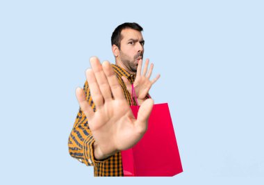 İzole mavi arka planda her iki eliyle stop jest yapma alışveriş çantaları ile adam