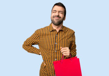 İzole mavi arka plan üzerinde bir çaba yapılmış olması için sırt ağrısı muzdarip alışveriş çantaları ile adam