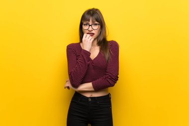 Sarı duvar üzerinde gözlüklü kadın gergin ve ağzına el koyarak korkuyor