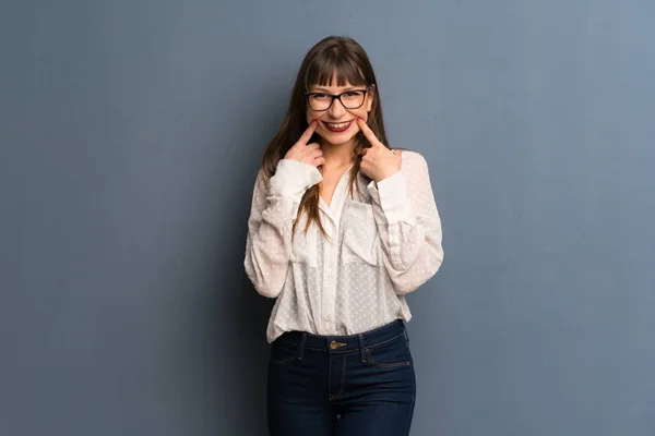 Woman with glasses over blue wall smiling with a happy and pleasant expression