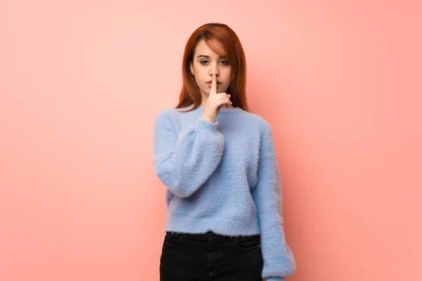 Young redhead woman over pink background showing a sign of silence gesture putting finger in mouth