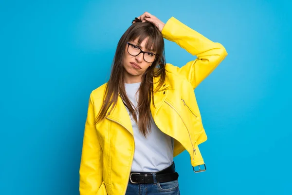 Young woman with yellow jacket on blue background with an expression of frustration and not understanding