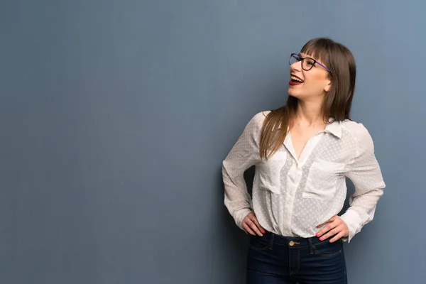 Kobieta Okularach Nad Niebieską Ścianę Stwarzające Bronią Biodrze Śmiechem — Zdjęcie stockowe