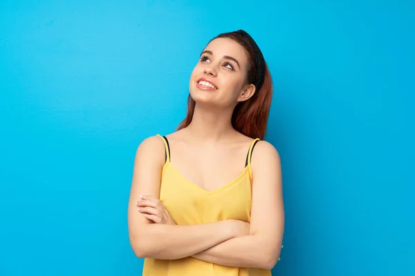 Joven Pelirroja Sobre Fondo Azul Mirando Hacia Arriba Mientras Sonríe — Foto de Stock