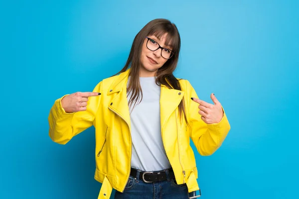 Young woman with yellow jacket on blue background proud and self-satisfied in love yourself concept