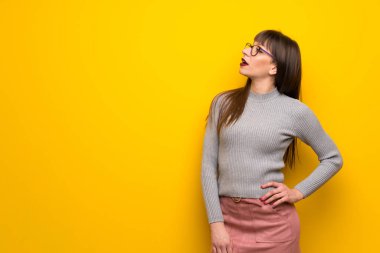 Kalça, silah ile poz ve gülen sarı duvarın üzerinden gözlüklü kadın