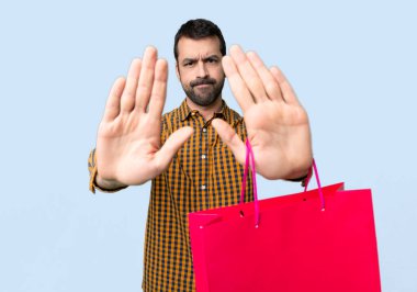 İzole mavi arka plan üzerinde bir görüş ile hayal kırıklığına için Stop jest yapma alışveriş çantaları ile adam