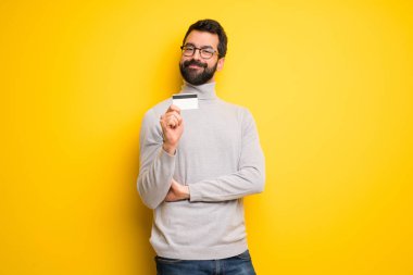 Bir kredi kartı tutan sakal ve balıkçı yakalı adam