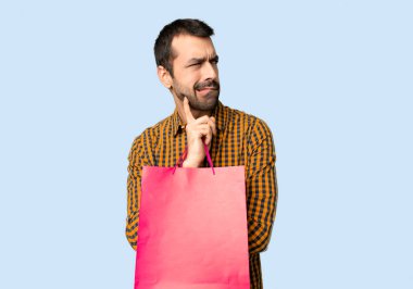 İzole mavi arka planda ısırık dudak yaparken yüz ifadesi karıştırır ile alışveriş çantaları ile adam