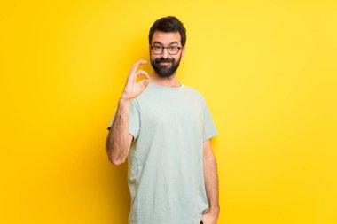 Parmaklar ok işaretiyle gösterilen sakallı ve yeşil gömlek adamla