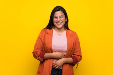 Kolombiyalı genç kız çok giyerken gülümseyen sarı duvarın üzerinden göğsüne eller