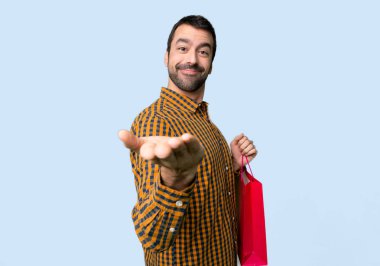 İzole mavi arka planda bir reklam eklemek için palmiye üzerinde boşaltmak hayali tutan alışveriş çantaları ile adam