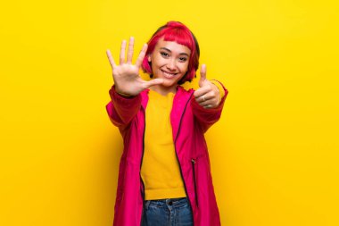 Altı parmaklı sayma sarı duvarın üzerinden pembe saçlı genç kadın