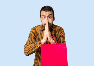 Alışveriş çantaları olan adam avuç içi tutar. Kişi izole mavi arka planda bir şey sorar