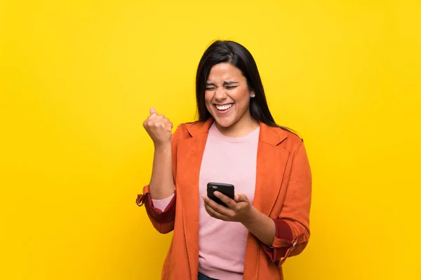 Joven Colombiana Sobre Muro Amarillo Celebrando Una Victoria Con Móvil — Foto de Stock