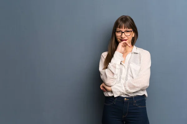 Woman with glasses over blue wall smiling and looking to the front with confident face