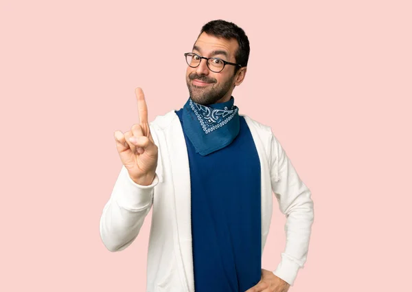 Handsome man with glasses showing and lifting a finger in sign of the best on isolated pink background