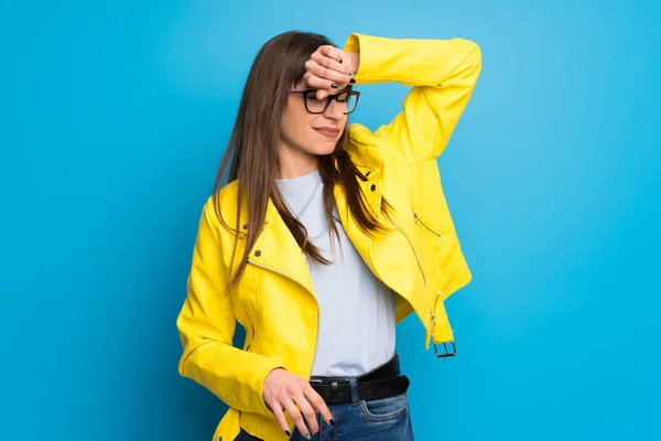 Young woman with yellow jacket on blue background with tired and sick expression