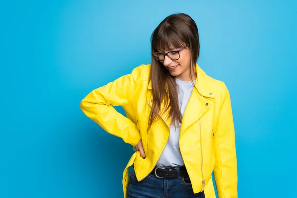 Young woman with yellow jacket on blue background happy and smiling
