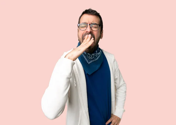 Handsome man with glasses yawning and covering wide open mouth with hand on isolated pink background
