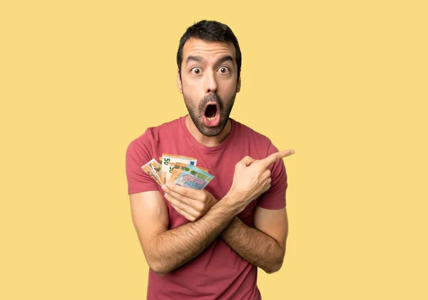 Hombre Tomando Montón Dinero Sorprendido Apuntando Lado Sobre Fondo Amarillo — Foto de Stock