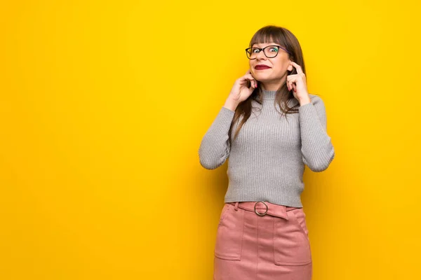 Žena Brýlemi Nad Žluté Stěny Pokrývá Obě Uši Rukama — Stock fotografie
