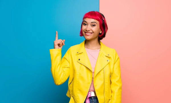 Young woman with yellow jacket showing and lifting a finger in sign of the best