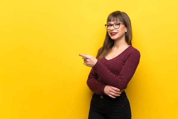 横に指を向ける黄色い壁の上に眼鏡をかけた女性 — ストック写真