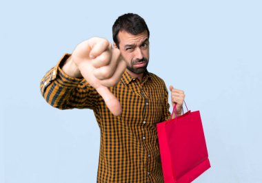 İzole mavi arka planda negatif ifade ile başparmak aşağı işareti gösteren alışveriş çantaları ile adam