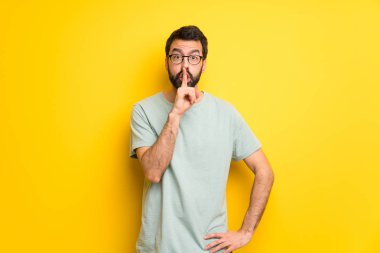 Sakallı ve yeşil gömlek bir işaret parmağını ağzına koyarak sessizlik jest gösteren adamla