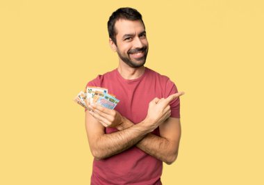 Adam izole sarı arka planda bir ürün sunmak için yan işaret çok para alarak