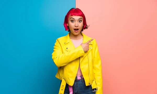 Young woman with yellow jacket surprised and pointing side