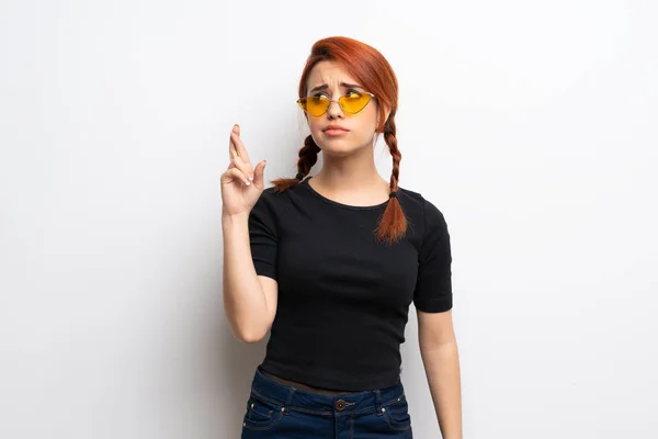 Young redhead woman over white wall with fingers crossing and wishing the best