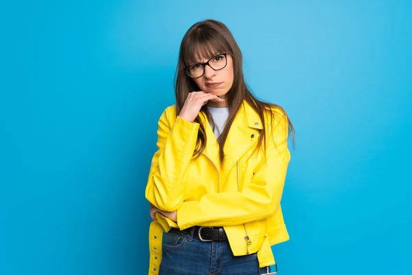 Young woman with yellow jacket on blue background having doubts