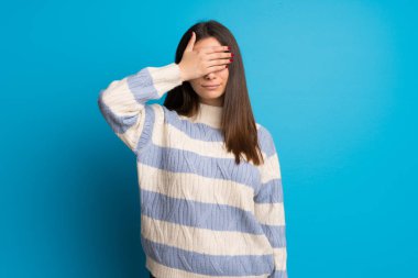 Mavi duvarın üzerindeki genç kadın gözleri elleriyle örtmek. Bir şey görmek istemiyorum