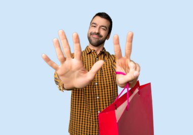 İzole mavi arka planda parmakları ile yedi sayma alışveriş çantaları ile adam