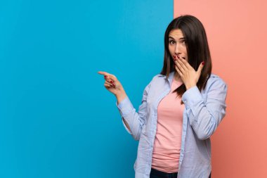 Pembe ve mavi duvar üzerinde genç kadın bir sürpriz yüz ile yan parmak işaret