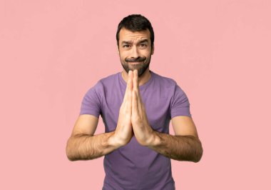 Handsome man keeps palm together. Person asks for something on isolated pink background clipart