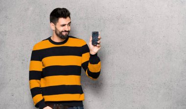 Kırık smartphone dokulu duvar'ın üstüne holding ile çizgili kazaklı yakışıklı adam sorunlu