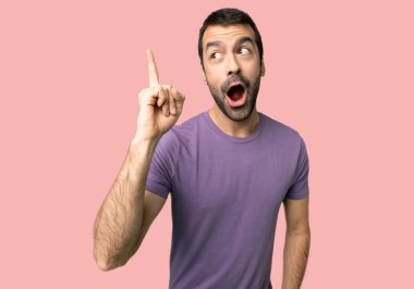 İzole pembe arka planda bir parmak kaldırırken çözümü fark etmek isteyen yakışıklı adam