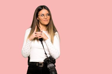 İzole pembe bir arka plan üzerinde bir şey entrikacı genç fotoğrafçı kadın