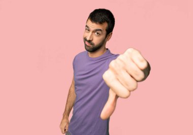 İzole pembe arka planda negatif ifade ile başparmak aşağı işareti gösteren yakışıklı adam