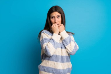 Mavi duvar üzerinde genç kadın biraz gergin ve ağzına eller koyarak korkuyor