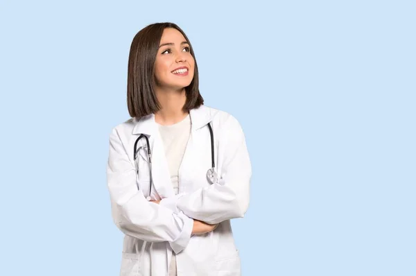 Jonge Dokter Vrouw Opzoeken Terwijl Glimlachend Geïsoleerde Blauwe Achtergrond — Stockfoto